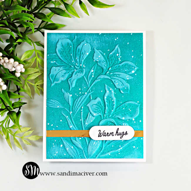 Handmade teal floral card featuring the Alstroemeria Blooms Embossing Folder with a subtle Blackout Technique, white paint splatters, a gold accent strip and a Warm Hugs sentiment.