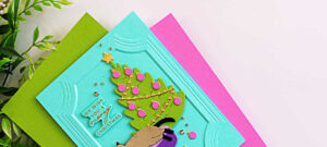 Close-up of a handmade Christmas card featuring a die-cut cat sleeping in a purple pet bed beside a decorated Christmas tree on a turquoise panel embossed with the A2 Ornate Molded Frame 3D Embossing Folder. The card includes a "We Wish You a Meowy Christmas" sentiment and is accented with gold embellishments and pink ornaments.