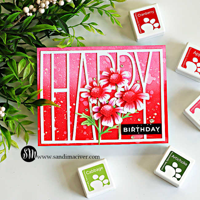 Ink blended happy birthday card featuring the Simon Says Stamp Tall Happy Cover Die over a pink ombré background blended with Rhubarb, Apple, and Cranberry inks. Layered Quirky Daisies create a bright floral focal point, accented with white paint splatter, sparkling gems, and a bold black birthday sentiment.