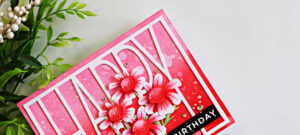 Close-up of an ink blended happy birthday card featuring the Simon Says Stamp Tall Happy Cover Die layered over a pink ombré background created with Rhubarb, Apple, and Cranberry inks. White Quirky Daisies are accented with pink ink blending, layered over the die-cut sentiment, and finished with white paint splatter, sparkling gems, and a black birthday sentiment.