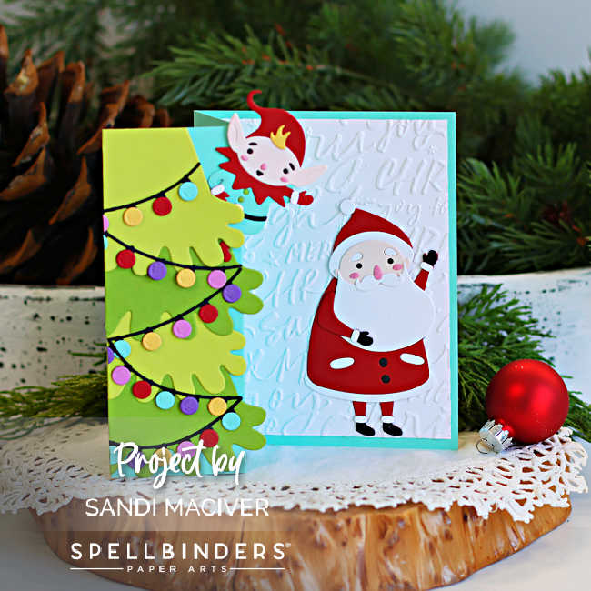 Front view of a handmade Merry Shuffle Single Z-Fold Christmas card featuring a layered green Christmas tree wrapped with colorful holiday lights, a playful elf peeking from behind the fold, and a die-cut Santa waving on a white embossed script background. The card is displayed on a rustic wood slice with evergreen branches, a pinecone, and a red Christmas ornament.
