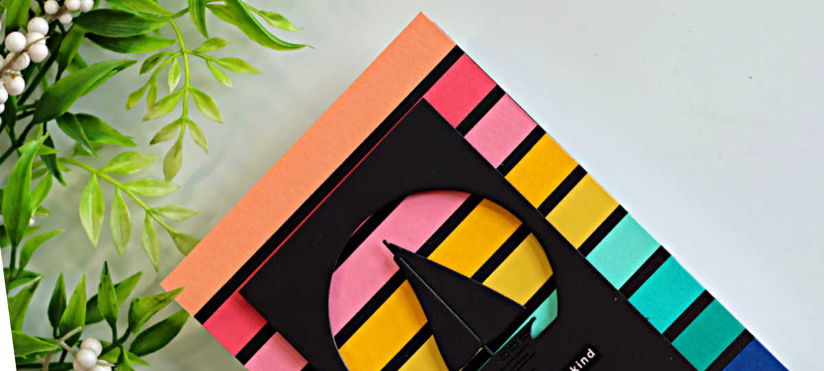 Close-up of a handmade retro sailboat card featuring colorful sunset-inspired cardstock stripes in coral, pink, yellow, aqua, and blue, with a black sailboat silhouette framed inside a circular die-cut window
