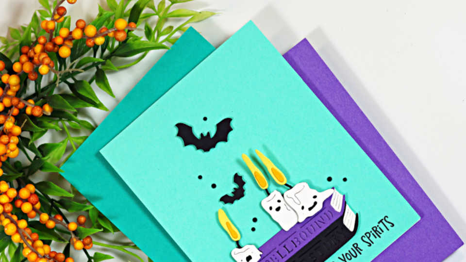 Handmade Halloween card featuring Spellbinders Boo Crew Lab dies with spooky books, dripping candles, ghosts and bats on a teal background.