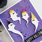 Simon Says Stamp STAMPtember Swirling Ghosts Halloween card featuring four white ghosts in colorful hats on a purple Distress Oxide background with pink and black splatters.
