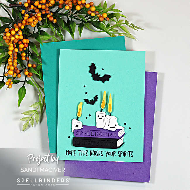 Handmade Halloween card featuring Spellbinders Boo Crew Lab dies with spooky books, ghost candles and flying bats on a teal background with purple accents.