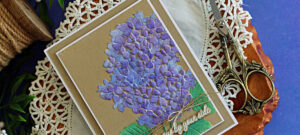 Handmade hydrangea card featuring purple stenciled flowers and green leaves on Kraft cardstock, layered with a white mat and finished with natural twine and an “Always by your side” sentiment.