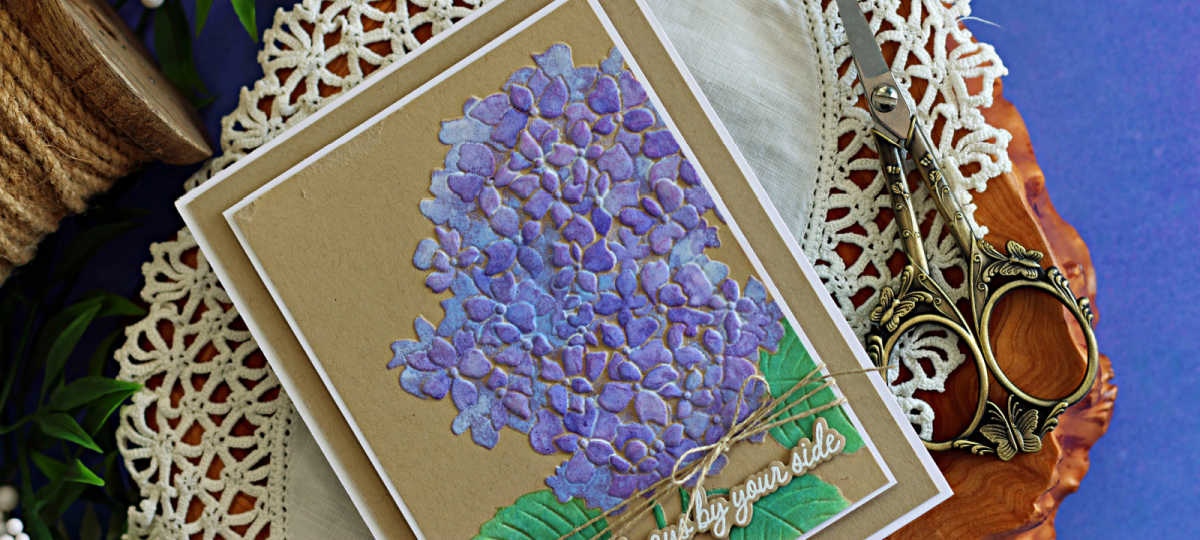 Handmade hydrangea card featuring purple stenciled flowers and green leaves on Kraft cardstock, layered with a white mat and finished with natural twine and an “Always by your side” sentiment.