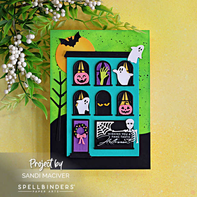 Fang-tastic Halloween card featuring a turquoise haunted house filled with ghosts, pink pumpkins, a spooky hand and skeleton, with a black tree and bright green ink-blended background.