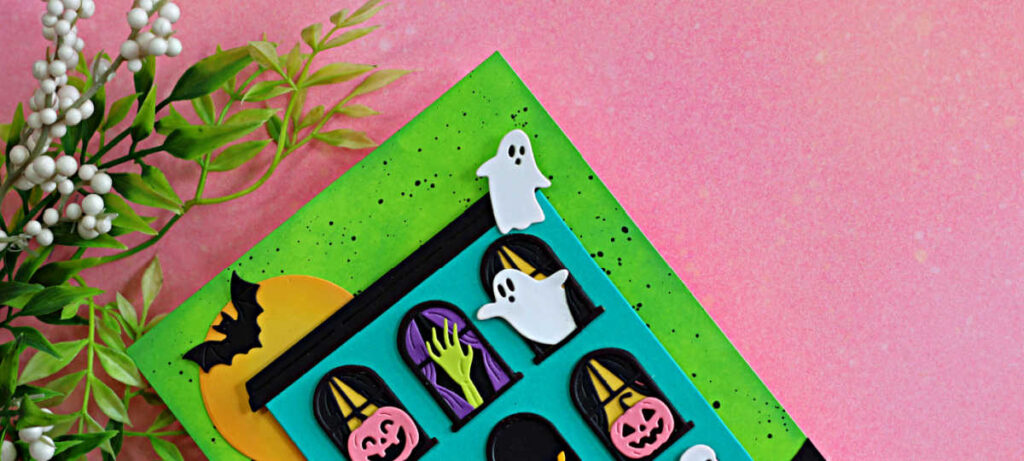 Colorful Halloween card featuring a turquoise haunted house with ghosts, pumpkins, bats and a spooky green hand against an ink-blended green background.