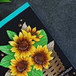 Close-up of a handmade birthday card featuring traditional golden yellow sunflowers in a woven basket, layered over a bold black Squarevel die-cut mat and teal card base.