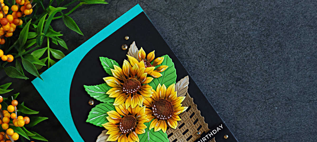 Close-up of a handmade birthday card featuring traditional golden yellow sunflowers in a woven basket, layered over a bold black Squarevel die-cut mat and teal card base.