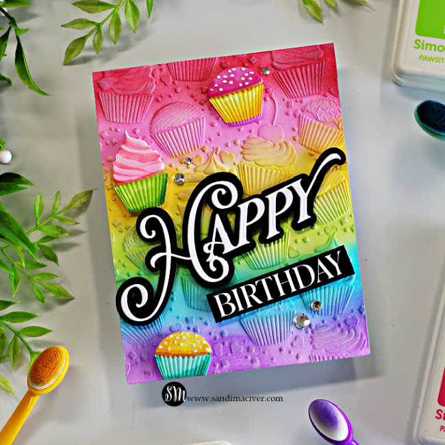 Rainbow ink-blended cupcake birthday card featuring an embossed cupcake background, dimensional cupcakes, and a large black-and-white Happy Birthday sentiment.