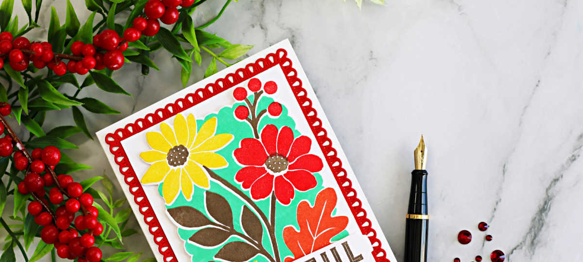 Close-up of a colorful Concord & 9th Incredibly Grateful floral card featuring red and yellow flowers, mint green background, and a decorative red die-cut frame, styled with red berries and a black fountain pen.