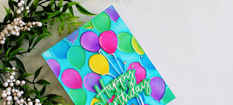 Close-up of a colorful birthday card featuring embossed party balloons in pink, purple, green, yellow, and blue against a turquoise background, finished with a layered Happy Birthday sentiment.