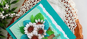 Close-up of a handmade Simon Says Stamp STAMPtember® card featuring white sunflowers and teal and green leaves in a dimensional woven basket, layered over an embossed mint background with aqua and white torn-edge borders.