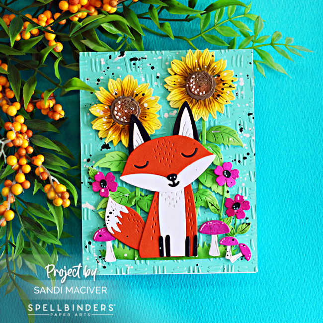 Spellbinders Hello Foxy fall card featuring a die-cut fox surrounded by sunflowers, bright pink flowers and mushrooms on a Waterfall embossed background.