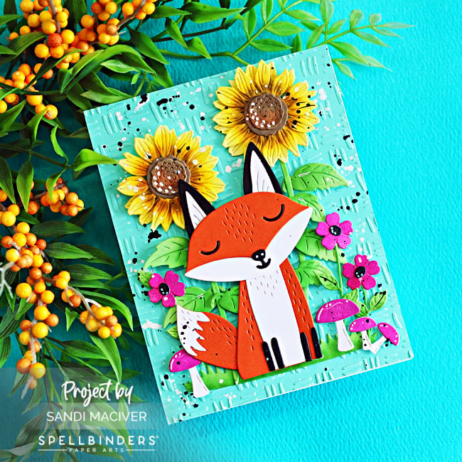 Spellbinders Hello Foxy fall card featuring a die-cut fox surrounded by sunflowers, bright pink flowers and mushrooms on a Waterfall embossed background.