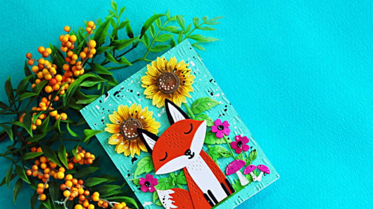 Spellbinders Hello Foxy fall card featuring a die-cut fox surrounded by sunflowers, bright pink flowers and mushrooms on a Waterfall embossed background.