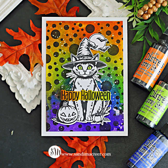 Halloween card featuring a witch cat, pumpkins, and bats on a rainbow Distress Spray background with black polka dots and a Happy Halloween sentiment.