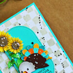 Fun Thanksgiving card featuring a colorful Too Much Turkey die cut, bright sunflowers, turquoise arches, and a stenciled check background with black splatter.