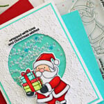 Simon Says Stamp and La-La Land Crafts Santa shaker card featuring a Copic-colored Santa, aqua shaker window, and embossed snowflake background.