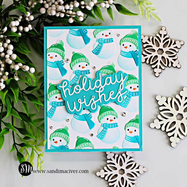 Cozy Snowman embossed and stenciled Christmas card featuring teal and green snowmen, a layered Holiday Wishes sentiment, sparkling gems, greenery, and snowflake accents.