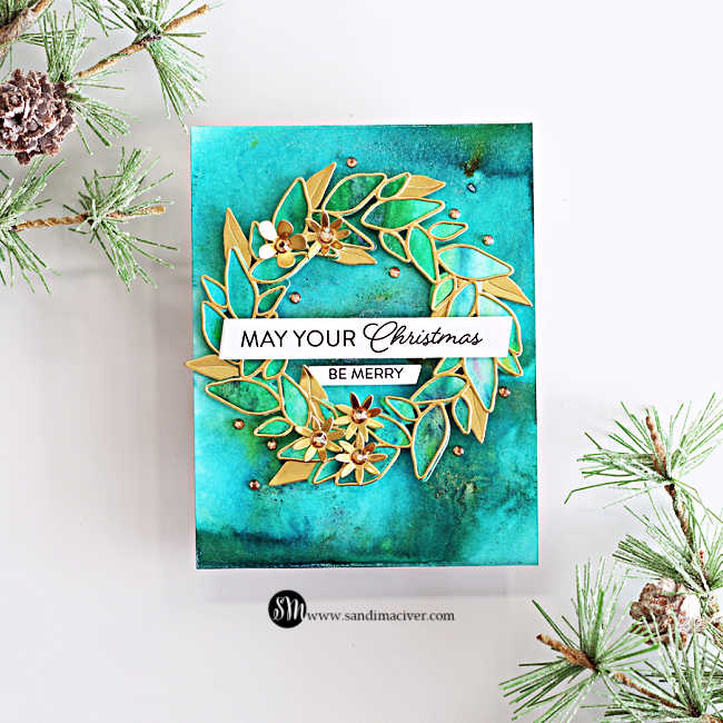 Leafy Wreath Christmas card featuring a gold die-cut wreath with teal and green leaves, gold flowers, and sparkling gems over a Lindy’s Magicals background, with a “May Your Christmas Be Merry” sentiment.