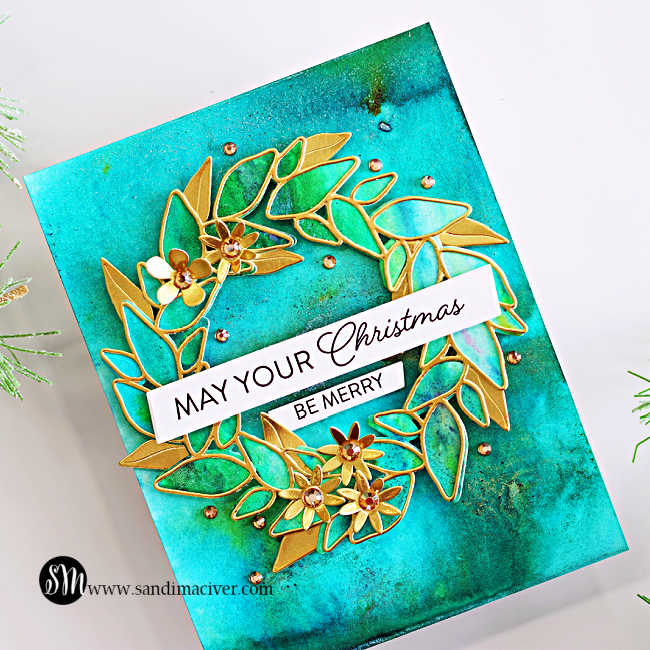 Close-up of a Leafy Wreath Christmas card with shimmering teal and green Lindy’s Magicals colors, matte gold leaves and flowers, sparkling gems, and a “May Your Christmas Be Merry” sentiment.