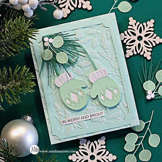 Mint Stitched Mittens Christmas card with white cuffs, die-cut greenery, and a Seafoam embossed background and frame, displayed on dark green with snowflakes and a silver ornament.