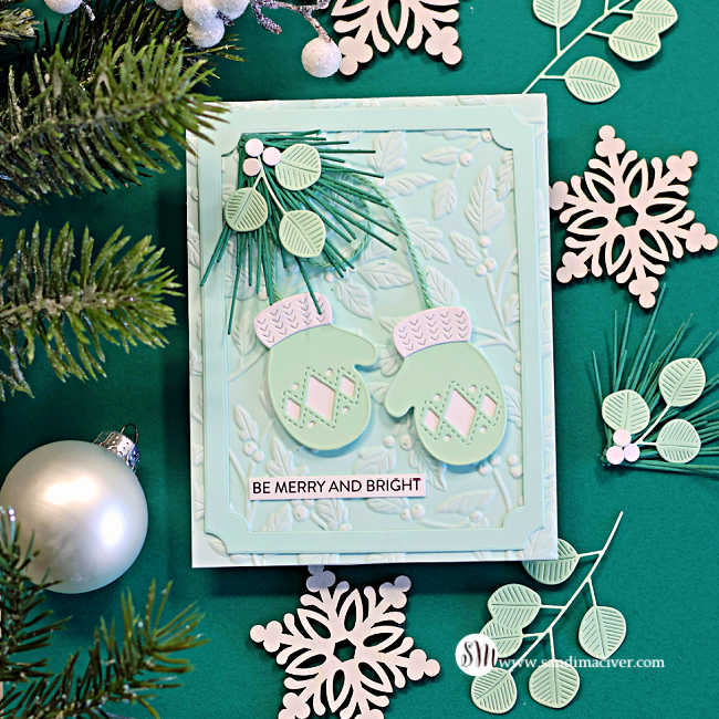 Stitched Mittens Christmas card featuring mint mittens with white cuffs, green twine, layered pine and eucalyptus sprigs, and white berries on a Seafoam embossed background with a “Be Merry and Bright” sentiment.