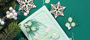 Mint Stitched Mittens Christmas card with white cuffs, layered die-cut greenery, a Seafoam embossed background and frame, and a “Be Merry and Bright” sentiment.