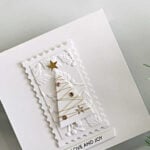 White-on-white Christmas card featuring a Simple Trees die-cut wrapped in gold thread, gold gems and stars, an embossed botanical panel, a postage-edge frame, and a “Love and Joy” sentiment.
