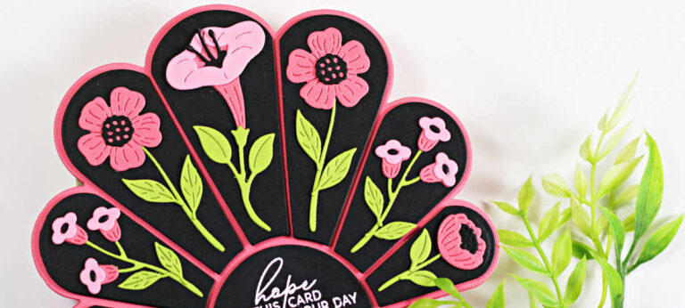 A handmade fan-shaped card created with the Spellbinders Small Die of the Month “Sunny Stems” set. The card features five arched black panels outlined in pink, each decorated with layered die-cut flowers in pink with bright green stems and leaves. A curved center panel includes a white heat-embossed sentiment that reads “hope this card brightens your day.” The card is photographed upright with greenery in the foreground.