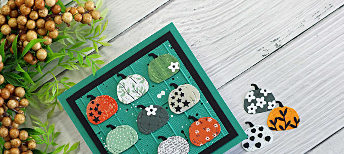 Handmade Thanksgiving card featuring nine patterned die-cut pumpkins on a teal embossed wooden plank background with black matting, including a pumpkin with repeating “thankful for you” text, photographed beside greenery and extra pumpkin die cuts.