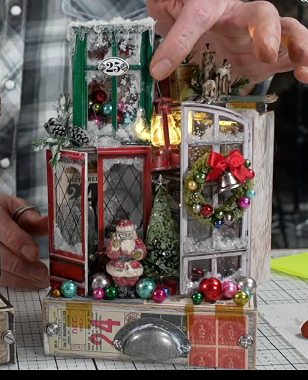 Christmas version of the Collector’s Laboratory featuring snowy red, green, and white cabinets, a miniature Santa, bottlebrush tree, glowing lantern, and an ornament wreath with a red bow and silver bells.
