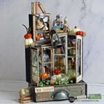 Tim Holtz Collector’s Laboratory Halloween assemblage featuring distressed miniature cabinets filled with tiny books, potion bottles, skulls, pumpkins, and a hanging lantern.