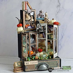 Tim Holtz Collector’s Laboratory Halloween assemblage featuring distressed miniature cabinets filled with tiny books, potion bottles, skulls, pumpkins, and a hanging lantern.
