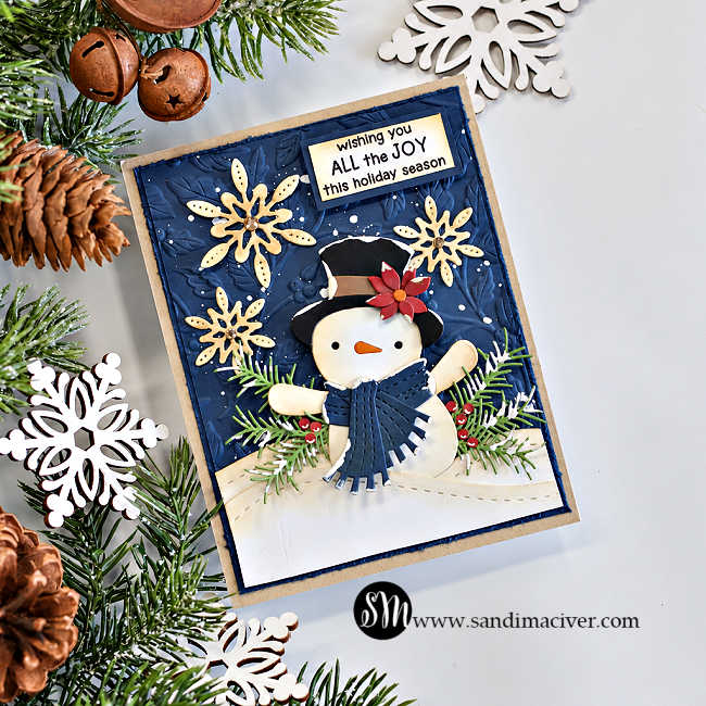 Angled view of a vintage masculine Christmas card featuring a snowman in a black top hat with a red poinsettia and navy scarf, cream snowflakes, evergreen sprigs, and snowy hills against an embossed navy background with white splatter.
